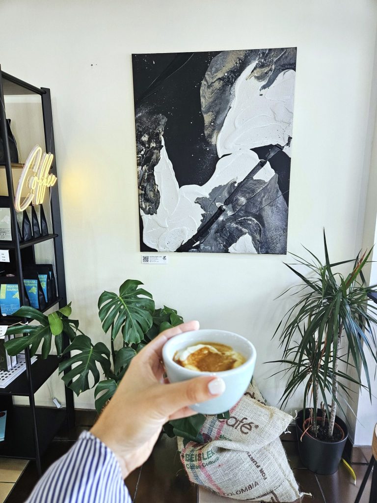 Tasse mit Kaffee in einer Hand vor einer modernen Wandkunst und grünen Pflanzen.