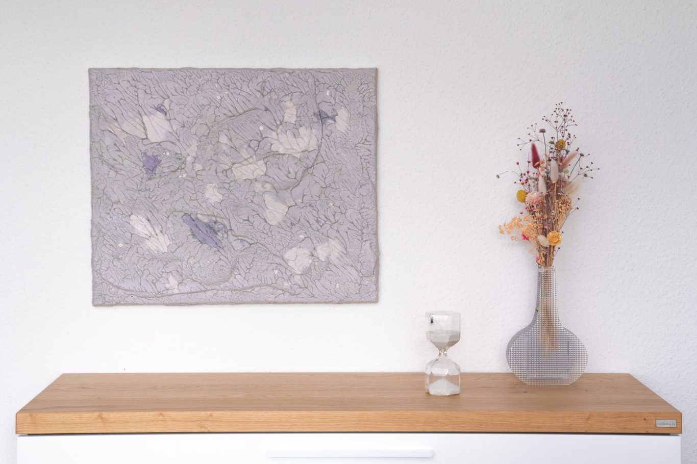 Perl, 50 x 60 cm, 300€* Abstrakte Wandkunst neben einer Vase mit getrockneten Blumen auf einem Holztisch.