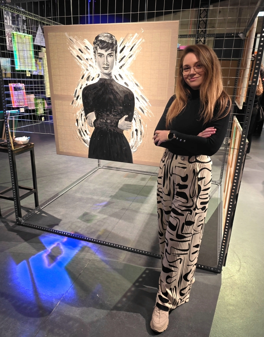Frau steht vor einem Kunstwerk mit einer stilisierten Abbildung einer anderen Frau.